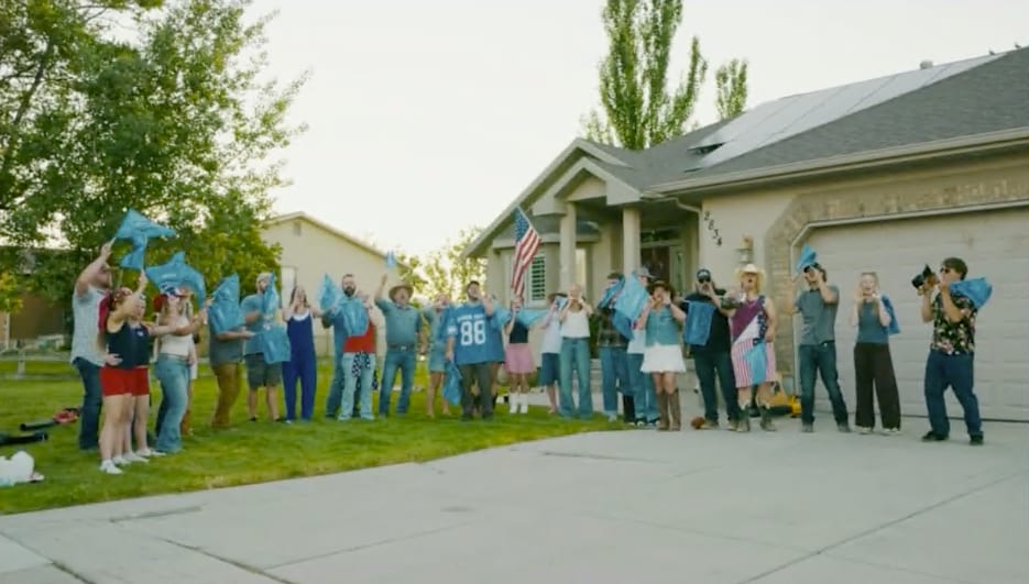 A community group holding blue flags in front of a residential home during the Bighorn Roofing 'Check Your Roof' music video campaign in Utah.